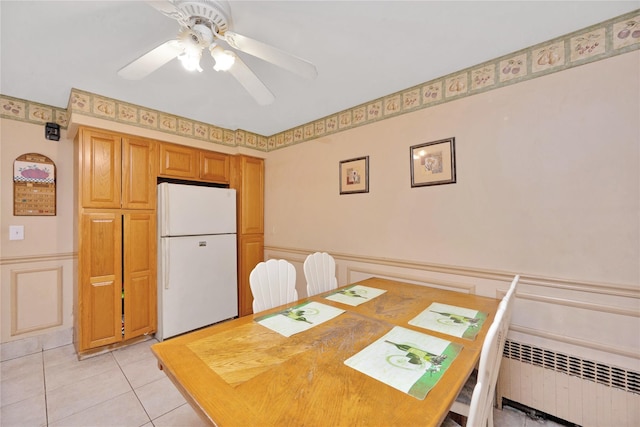 dining room featuring radiator, light tile patterned floors, wainscoting, a decorative wall, and a ceiling fan