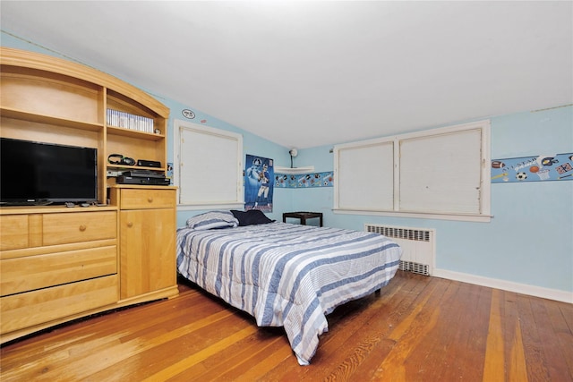 bedroom featuring hardwood / wood-style floors, lofted ceiling, radiator, and baseboards