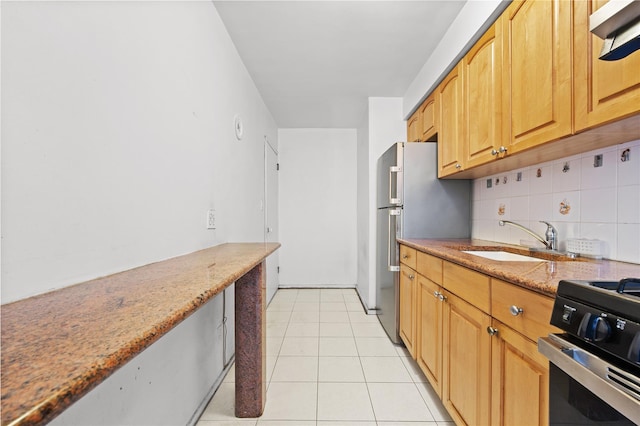 kitchen featuring range with gas stovetop, light stone counters, light tile patterned floors, a sink, and backsplash