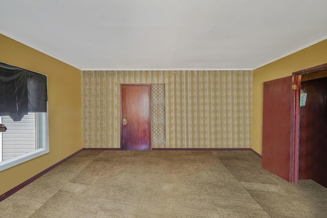 carpeted empty room featuring wallpapered walls, crown molding, and baseboards