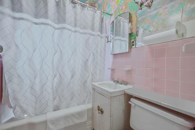 bathroom with wallpapered walls, shower / bath combo with shower curtain, toilet, vanity, and tile walls