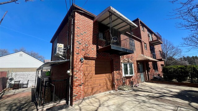 view of home's exterior with driveway, brick siding, a balcony, and an attached garage