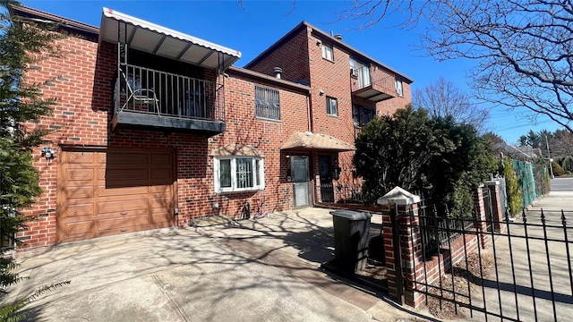 view of front facade featuring a balcony, fence, driveway, an attached garage, and brick siding