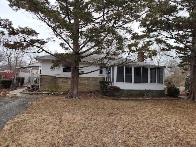 view of property exterior featuring fence, stone siding, a sunroom, and a chimney