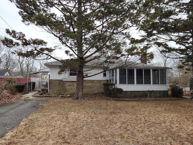 view of side of home with stone siding, a chimney, fence, and a sunroom