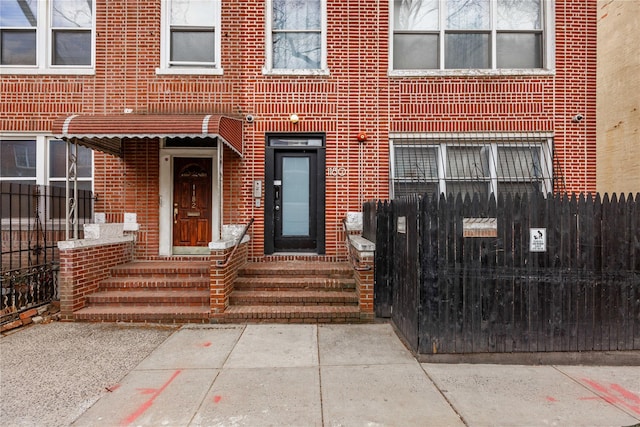 property entrance featuring elevator, fence, and brick siding
