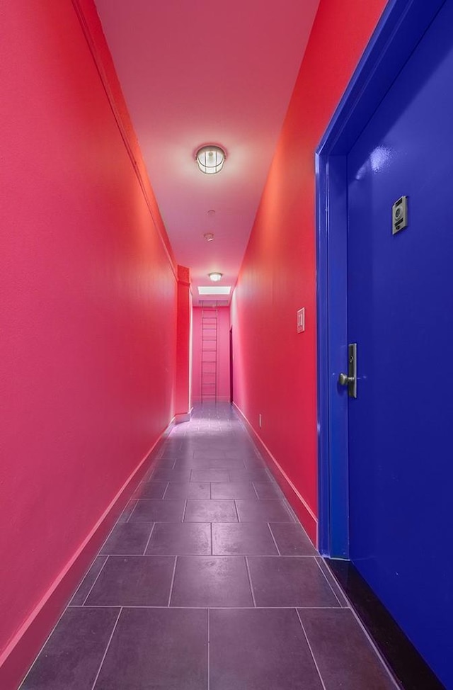 hallway with dark tile patterned floors and baseboards