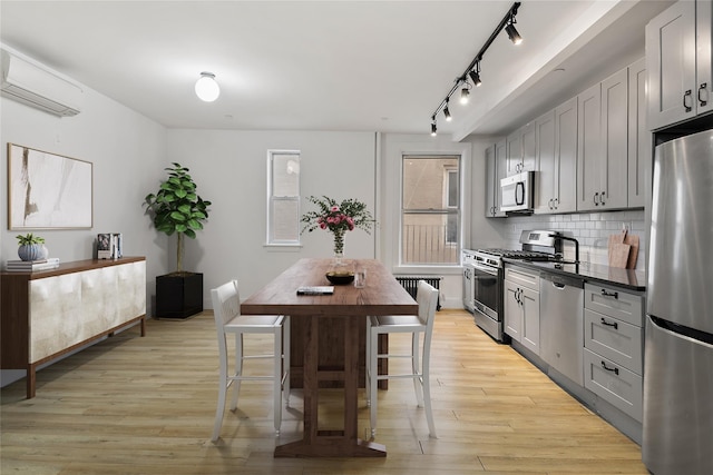 kitchen with a wall mounted air conditioner, light wood-type flooring, gray cabinetry, tasteful backsplash, and stainless steel appliances