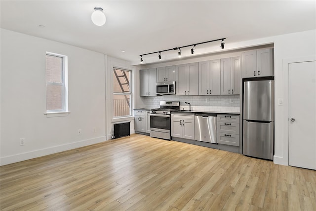 kitchen featuring backsplash, radiator heating unit, gray cabinets, and appliances with stainless steel finishes