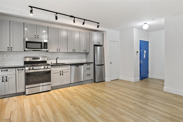 kitchen featuring a sink, stainless steel appliances, dark countertops, light wood-type flooring, and backsplash
