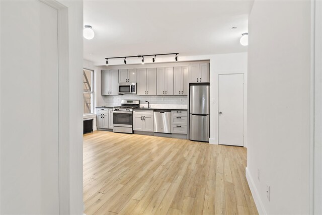 kitchen featuring tasteful backsplash, gray cabinets, appliances with stainless steel finishes, light wood-style floors, and a sink