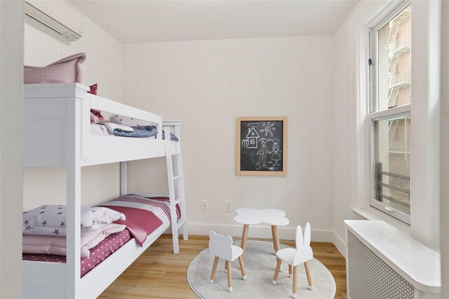 bedroom featuring radiator, wood finished floors, baseboards, and a wall mounted AC
