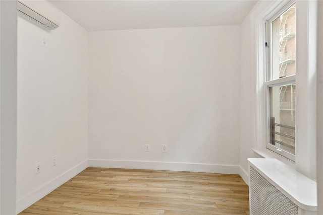 spare room with radiator, an AC wall unit, light wood-type flooring, and baseboards