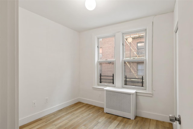 empty room featuring light wood-style flooring, radiator heating unit, and baseboards