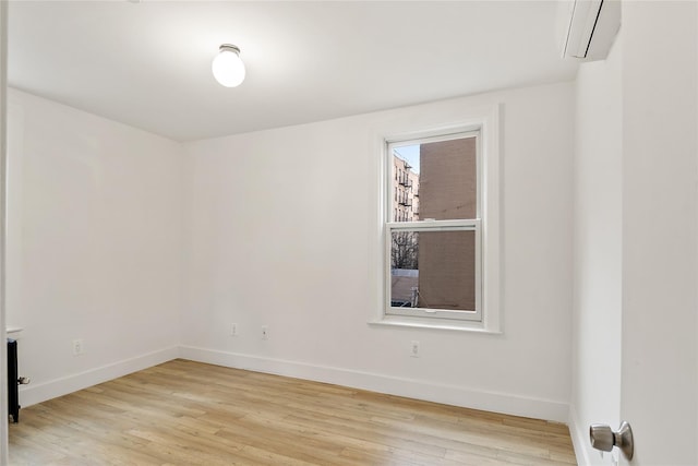 unfurnished room featuring baseboards, light wood-type flooring, and a wall mounted AC