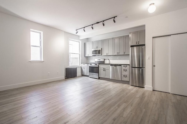 kitchen featuring radiator, light wood finished floors, gray cabinets, appliances with stainless steel finishes, and tasteful backsplash