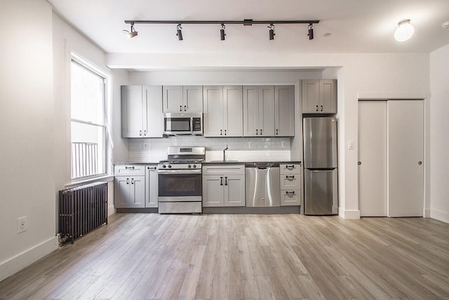 kitchen with radiator heating unit, light wood-style floors, gray cabinets, and appliances with stainless steel finishes