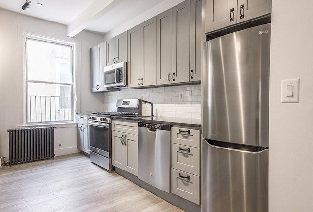 kitchen featuring radiator heating unit, gray cabinetry, appliances with stainless steel finishes, dark countertops, and backsplash