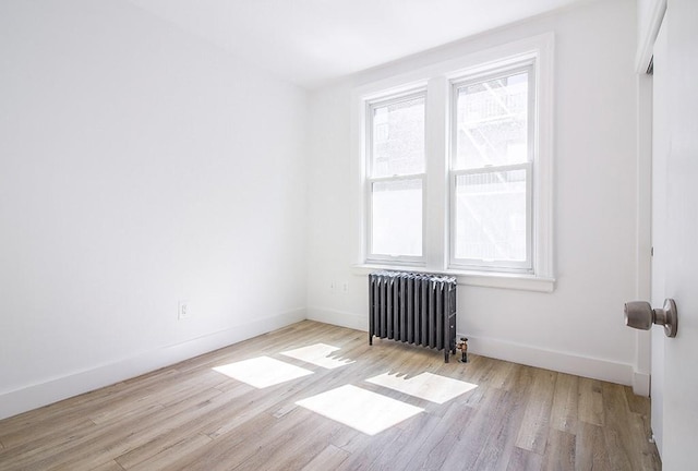empty room featuring baseboards, wood finished floors, and radiator heating unit