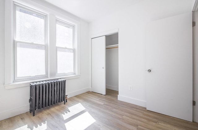 unfurnished bedroom featuring radiator heating unit, wood finished floors, baseboards, and a closet