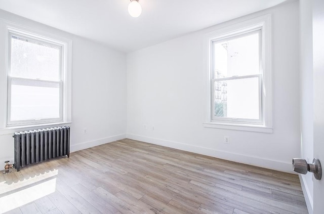 spare room with baseboards, radiator, and light wood-style flooring