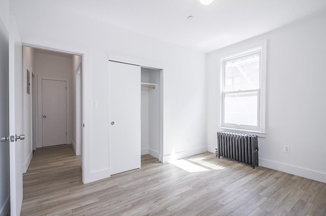 unfurnished bedroom featuring a closet, radiator heating unit, baseboards, and light wood finished floors