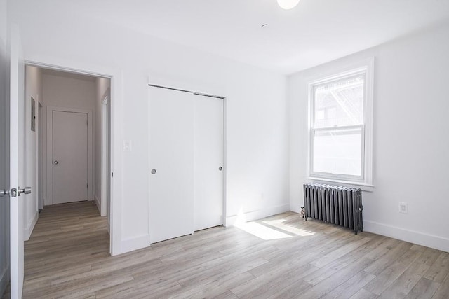 unfurnished bedroom with light wood-style flooring, radiator, baseboards, and a closet