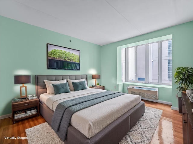 bedroom with multiple windows, wood finished floors, baseboards, and a wall mounted air conditioner