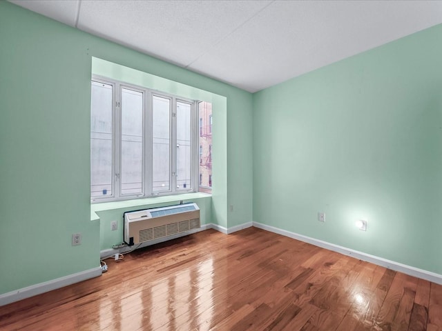 spare room with a wall mounted AC, baseboards, and wood finished floors