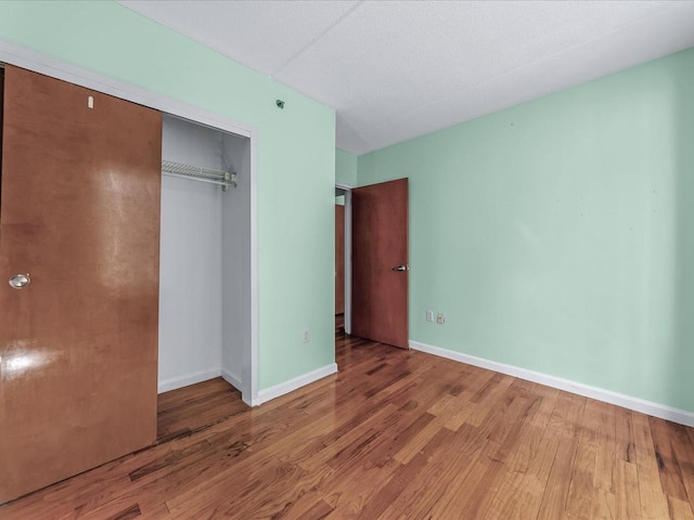 unfurnished bedroom featuring wood finished floors, a closet, and baseboards