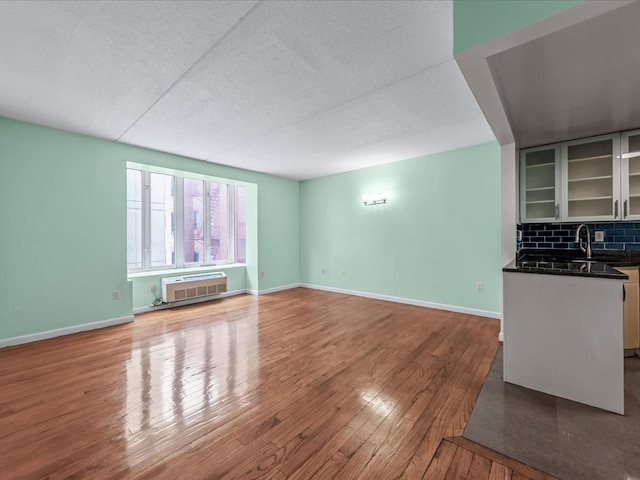 unfurnished living room with a wall mounted air conditioner, baseboards, wood-type flooring, and a textured ceiling