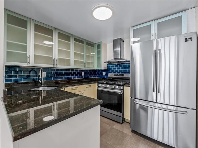 kitchen with backsplash, wall chimney range hood, dark stone counters, stainless steel appliances, and a sink