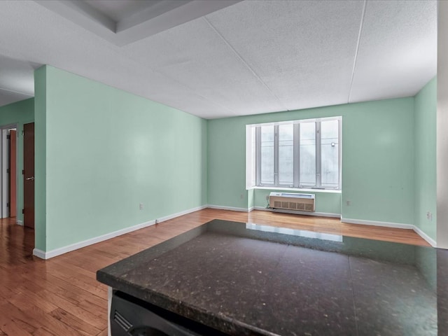 interior space featuring wood finished floors, baseboards, a wall mounted air conditioner, and a textured ceiling