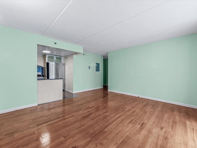 unfurnished living room featuring electric panel, baseboards, and wood finished floors