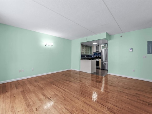 unfurnished living room with electric panel, baseboards, and wood finished floors