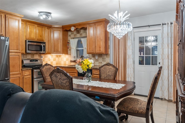 kitchen featuring light tile patterned floors, decorative backsplash, hanging light fixtures, appliances with stainless steel finishes, and a chandelier