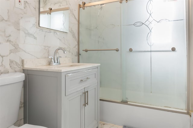 full bathroom with toilet, vanity, shower / bath combination with glass door, marble finish floor, and tile walls