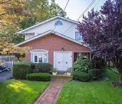 view of front of house featuring brick siding, a front lawn, and fence