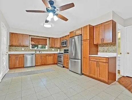 kitchen featuring decorative backsplash, light countertops, brown cabinets, and stainless steel appliances