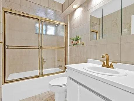 bathroom featuring enclosed tub / shower combo, toilet, tile walls, and vanity