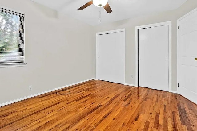 unfurnished bedroom with a ceiling fan, wood finished floors, baseboards, and two closets