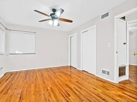 unfurnished bedroom with wood finished floors, visible vents, two closets, and ceiling fan