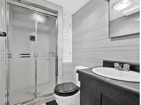 bathroom with toilet, a stall shower, tile walls, and vanity