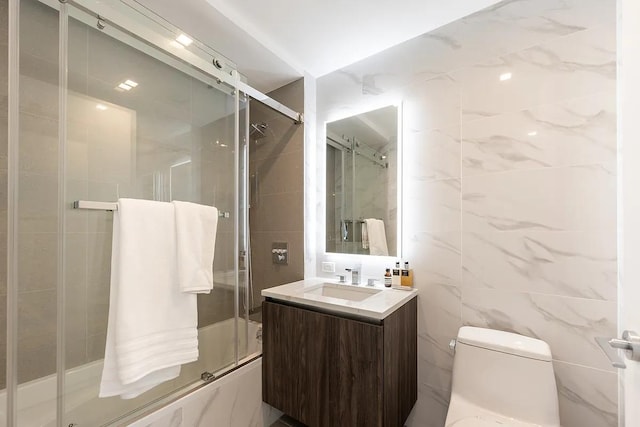 bathroom with vanity, toilet, tile walls, and shower / bath combination with glass door