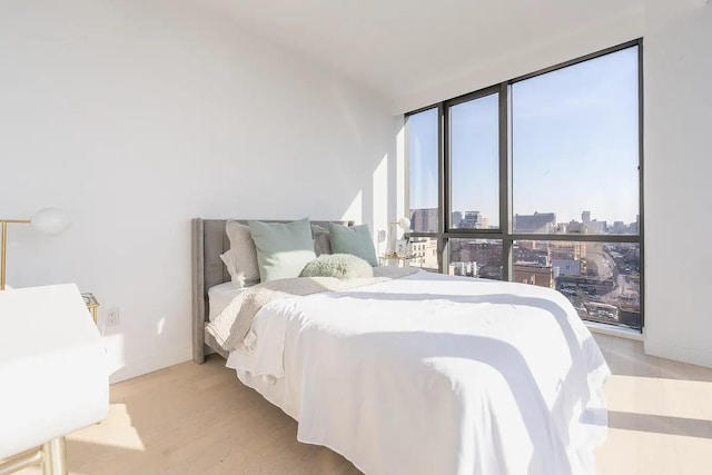 bedroom with baseboards, a view of city, wood finished floors, and floor to ceiling windows