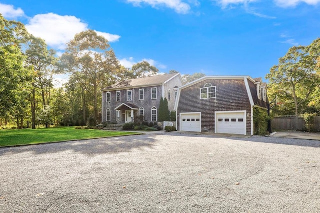 colonial house featuring a gambrel roof, a front lawn, fence, gravel driveway, and a garage