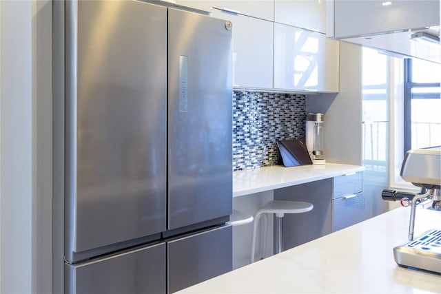 kitchen featuring modern cabinets, freestanding refrigerator, white cabinets, light countertops, and decorative backsplash