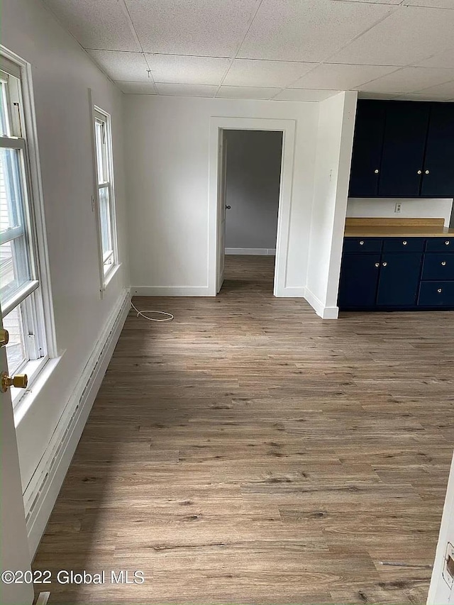 empty room with baseboards, a drop ceiling, a healthy amount of sunlight, and wood finished floors