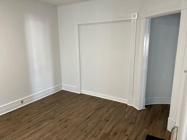 unfurnished bedroom featuring baseboards, dark wood-style floors, ornamental molding, and a closet