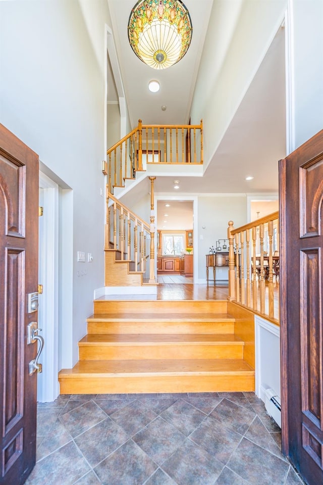 entryway with stairway, baseboard heating, and a towering ceiling